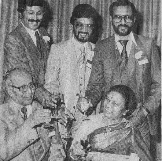 Black and white photo of Sivalinga Dass and his wife raising glasses, with three of their sons standing behind them